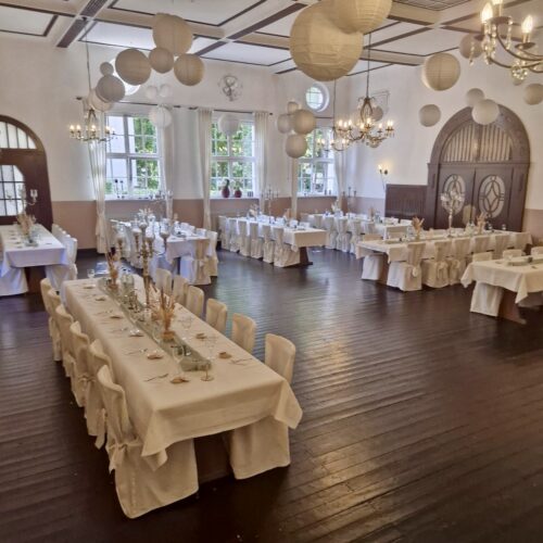 Eleganter Festsaal mit weißen Tischdecken, hängenden Laternen und gedeckten Tafeln.