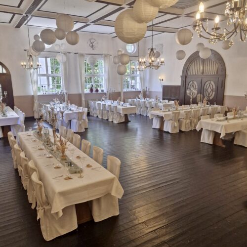 Eleganter Saal mit weißen Tischdecken, Kronleuchtern und hängenden Papierlaternen.